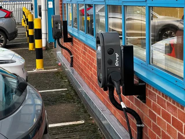 Row of twin-socket workplace chargers on wall brackets beside staff parking